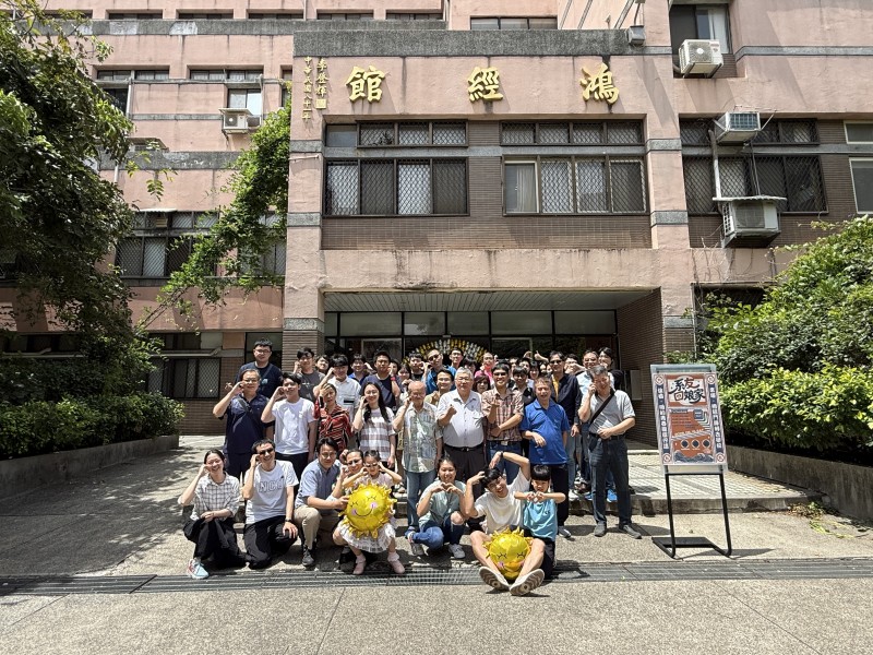 2026年5月16日系友回娘家大合照：數十位系友與師長在鴻經館大門前合影，前排有人抱著笑臉氣球，右側立著系友回娘家海報
